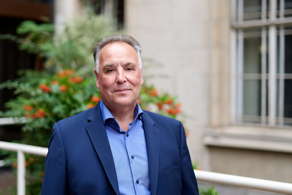 A man stands outside a large council building wearing a blue suit.